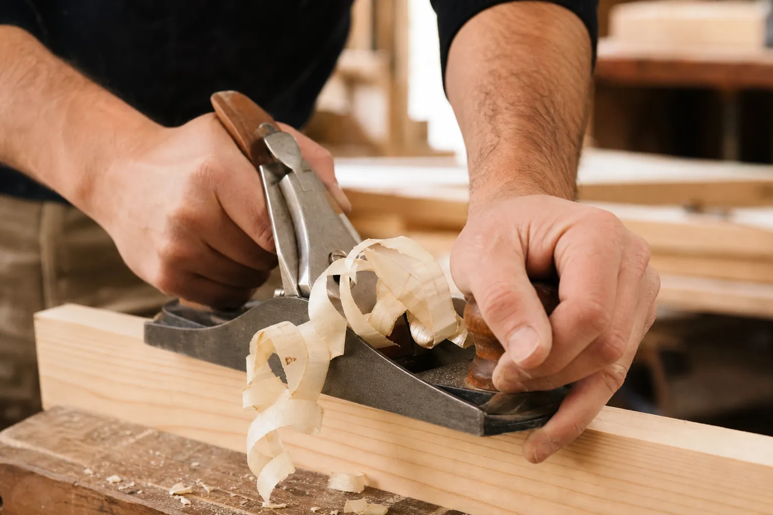 Mains d’un charpentier tenant un rabot sur une pièce de bois clair, geste de rabotage